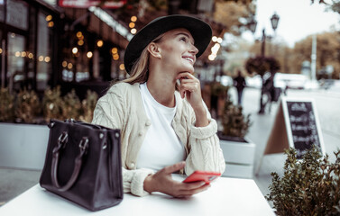 Cute fashion woman using smartphone while sitting at table in outdoor cafe. Lifestyle