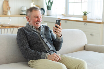 Obraz premium Happy middle aged senior man talk on video call with friends family. Laughing mature old senior grandfather having fun speaking with grown up children online. Older generation modern tech usage