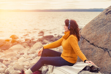 Happy woman listening to music wearing headphones and relaxing at sunset by the sea.