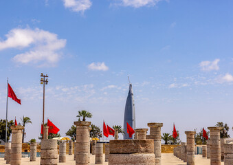 Remains of the unfinished Great Mosque in Rabat, Moroccan flags waving and the Mohammed VI Tower in the background.