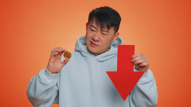 Asian man show golden bitcoins indicating red arrow banner down sign, decrease of exchange rate. Unsuccessful bankruptcy business, fall of stock cryptocurrency market investment mining BTC technology