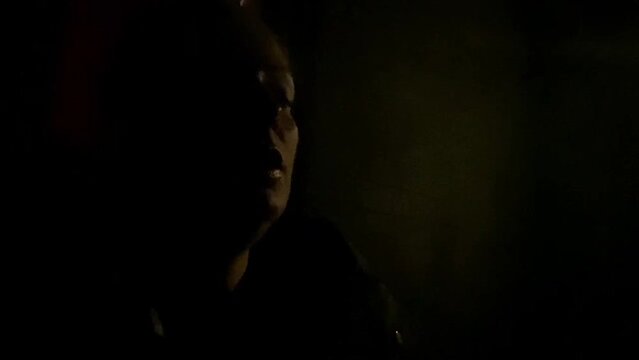 Woman smoking cigarette at night in dark with copy space, blowing cigarette smoke into light