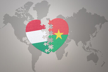 puzzle heart with the national flag of burkina faso and hungary on a world map background.Concept.