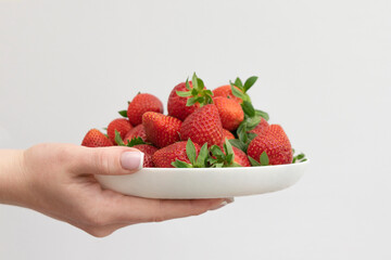 women hand hold a white bowl filled with straberries