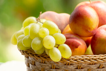 Fresh ripe apples, peaches, green and blue grapes in basket. Healthy food on table on defocus autumn background.