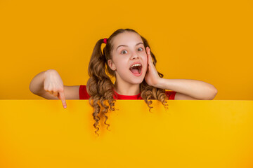 surprised child behind blank yellow paper with copy space for advertisement. point finger