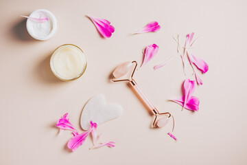 Rose quartz roller, gua sha and face creams on pink background, spa treatments.