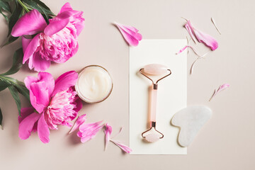 Roller and gua sha rose quartz, cream and pink peony flowers. Spa concept.