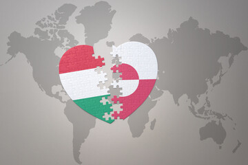 puzzle heart with the national flag of greenland and hungary on a world map background.Concept.