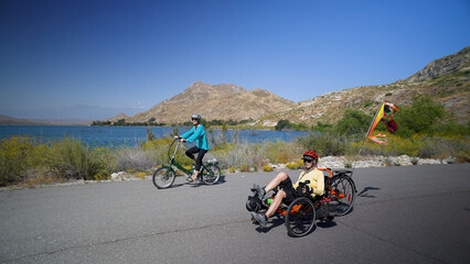 Mother and daughter biking together riding recumbent and normal electric e bikes next to lake and mountains.