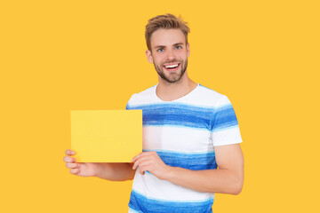 Fototapeta premium man smile offer product advertisement. man holds paper with special offer advertisement. man show advertisement and offer promotion isolated on yellow. man sales representative offer advertisement