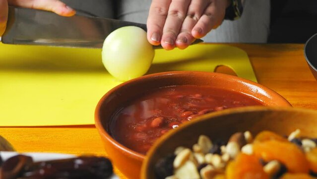 Women's hands cut onion for cholent with a large knife on a plastic board. close-up