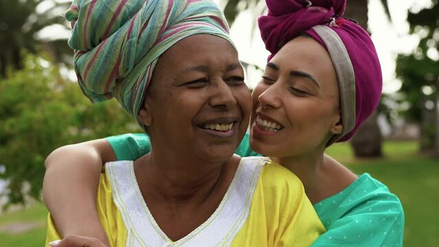 African mother and adult daughter wearing traditional dress and having tender moment at nature park - Family love concept