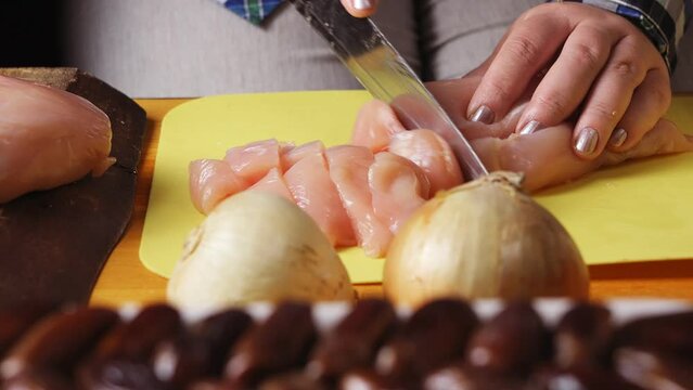 Women's hands cut chicken for cholent with a large knife on a plastic board. close-up