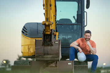 Builder with excavator for construction at the construction site. Machinery tractor with builder at buildings background. Excavator builder worker. Builder with helmet on construction site.