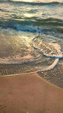 Sea waves rolling on sandy shore beach on sea coast at dawn sunset. Blue sea waves with white foam roll coming on sand beach. Seaside seashore seaboard shoreline. Natural background, nature. Vertical