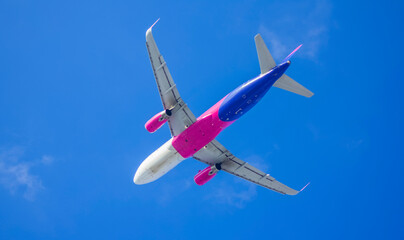 A white-blue-pink plane flies on a journey against a clear sky during the day. Air travel, tourism, aviation, jet twin-engine civil airliner