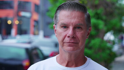 Portrait of a serious middle-aged man standing in city street looking at camera with neutral...