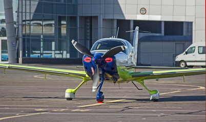 A small, privately owned, propeller-driven, white-green-blue pleasure plane is parked at the...