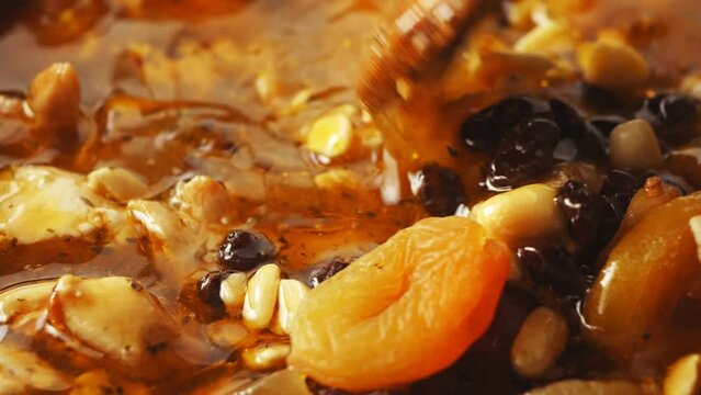 Pieces of chicken fried in a cast-iron skillet in oil with onions and spices and dried fruits cholent are mixed with a spatula. Close-up