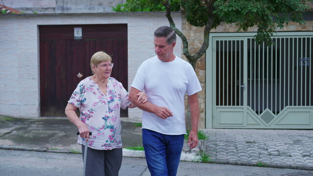 Middle-aged son assisting elderly mother to walk. Man caring and supporting senior person. Old age domestic lifestyle routine