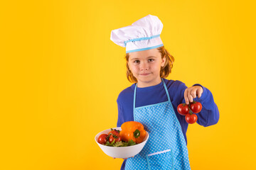 Kid cook hold tomato. Chef kid boy in form of cook. Child boy with apron and chef hat preparing a healthy meal in the kitchen. Cooking process.