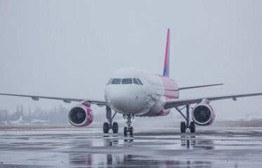 
Pink-lilac-white twin-engine passenger plane rides on the taxiway to take off in winter, flying in bad weather, the plane is preparing to take off, flying in winter
