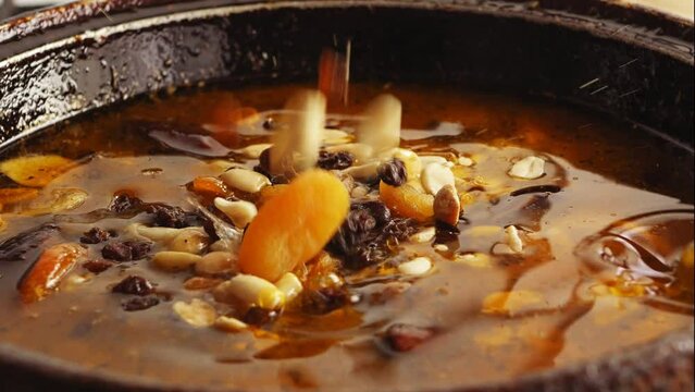 Pieces of chicken fried in a cast-iron skillet in oil with onions and spices in the broth, and dried fruits and nuts fall. Close-up