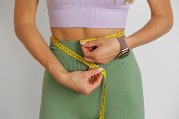 Slim woman measuring her waist by measure tape. Close up. Workout, sport, motivation concept