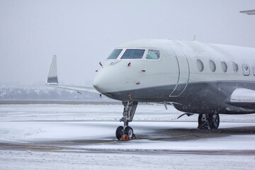 
Private white business jet jet stands at the airport under the snow in winter against a cloudy sky...