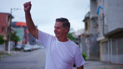 Happy older man waving hello to neighbors while walking in street. A middle-age caucasian male person walks forward toward camera while greeting to friends around him © Marco