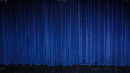 The theatrical curtain is closed, illuminated by deep blue spotlights.