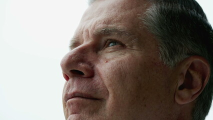 Contemplative older man close-up face looking up at sky with thoughtful expression, person closing eyes in meditation