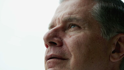 Contemplative older man close-up face looking up at sky with thoughtful expression, person closing eyes in meditation