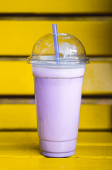 Purple milkshake in hands on yellow bench. Summer sweet cold drink.