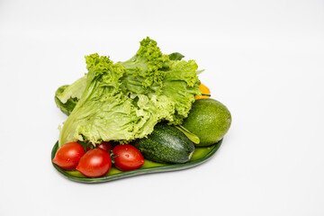 Bundle of  ripe fresh vegetables. Green lettuce, red cocktail tomatoes, avocadoes, lemons. White kitchen background.