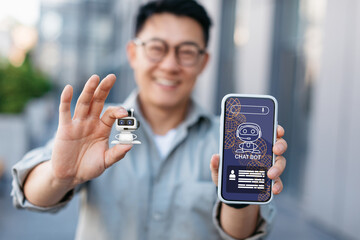 Happy chinese man holding robot and smartphone with chatbot