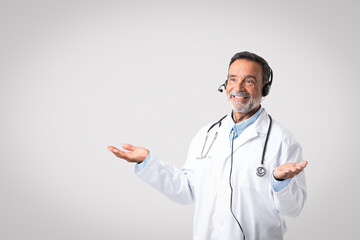 Happy caucasian mature man doctor therapist in white coat, headphones spreads arms to sides, hold...
