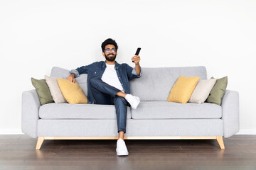 Relaxed indian guy enjoying weekend at home, watching TV