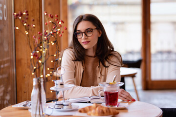 Attractive brunette haired woman sitting in a cafe next to window and daydreaming
