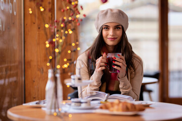 Beautiful woman wearing beret hat and scarf whle sitting in a cafe and reading a book