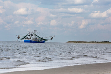 Obraz premium Shrimp boats off the shore of the Savannah River by the Atlantic Ocean with blue sky and white clouds.