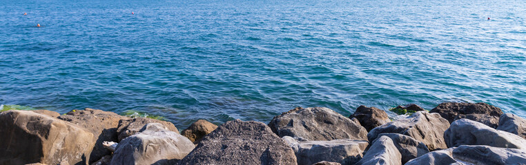 Tranquility rocky beach with big black stones, blue sea and sky as background, tranquil and looks beautiful.Big stone beach in front of sea with sky