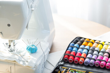 Sewing layout with multicolored spools of thread close-up, needles, electric sewing machine....