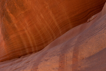 The face of a red sandstone cliff in Peekaboo Canyon, Utah is streaked with horizontal sedimentary lines and vertical oxidized lines where water has run down the cliff during rain storms.