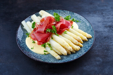 Traditionell gedämpfter weißer Spargel mit Rohschinken und Sauce Hollandaise serviert als Nahaufnahme auf einem Nordic Design Teller