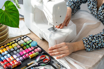 Woman hand close up sews tulle on electric sewing machine. Filling the thread into the sewing needle, adjusting the tension. Comfort in the house, a housewife's hobby, layout of sewing tools - obrazy, fototapety, plakaty