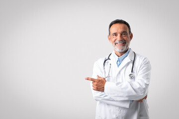 Happy caucasian senior doctor therapist in white coat point finger on free space