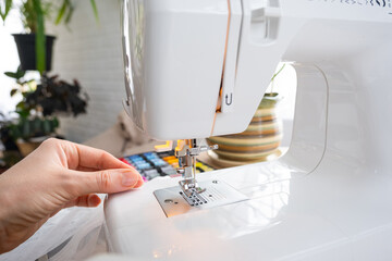 Woman hand close up sews tulle on electric sewing machine. Filling the thread into the sewing...