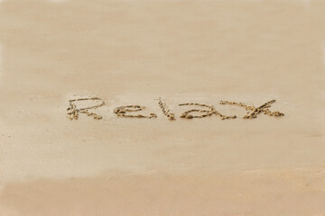 Relax word written in the wet sand of the beach. Healthy lifestyle.